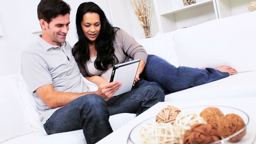 Attractive young heterosexual Hispanic couple relaxing on home couch with wireless tablet
