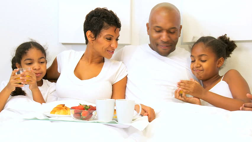 African American family relaxing sharing breakfast bed weekend