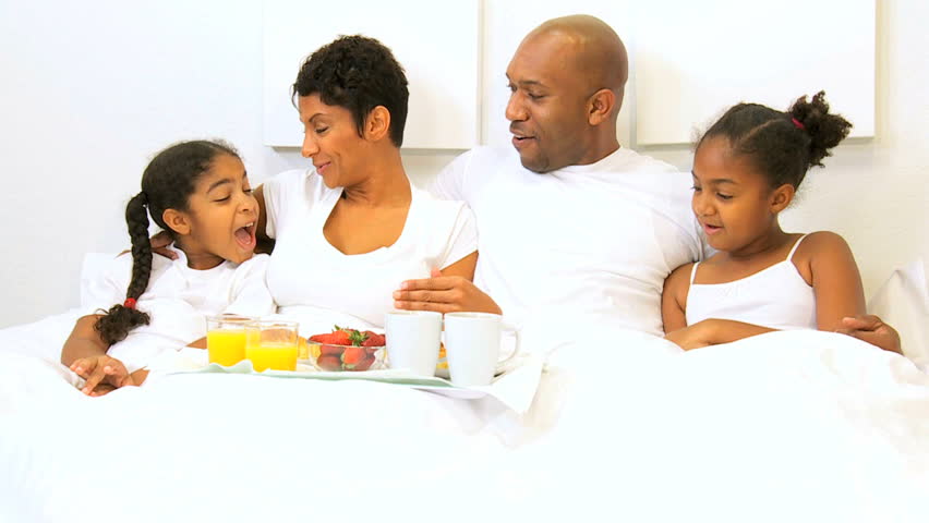 Ethnic parents children enjoying breakfast bed weekend