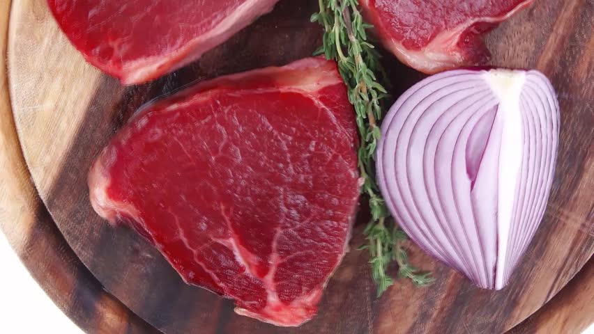 uncooked raw beef fillet with thyme twig on wooden plate isolated over white background