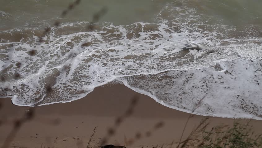 Ocean waves break on shore in shallow waters. Inflatable boat floats ahead.
