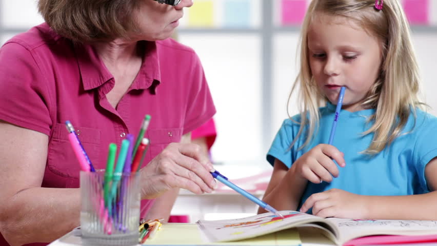 A kindergarten teacher helps her cute little student with her work.