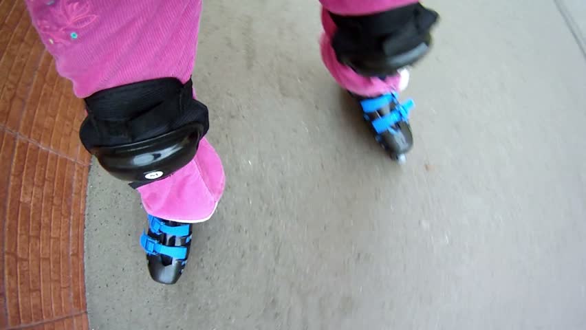 Little girl rollerblading on paved road near brick wall