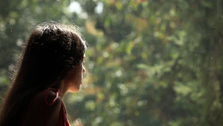 Young adult woman comes to window, sees someone outdoor and pulls the red drapes.
