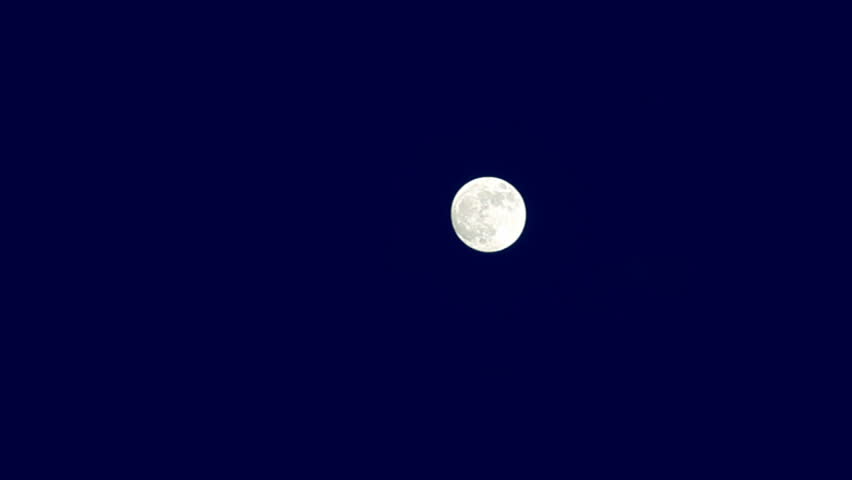Full moon rising through the clouds on dark blue evening sky. Time lapse, 30 second
