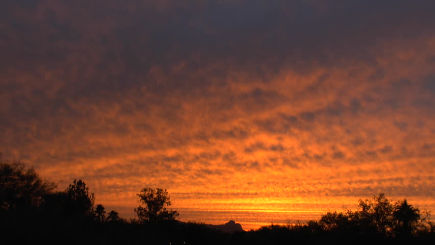 Time Lapse, Sweeping grey cloud engulfs vibrant, orange, red, streaked sunset above silhouetted landscape. 1080p