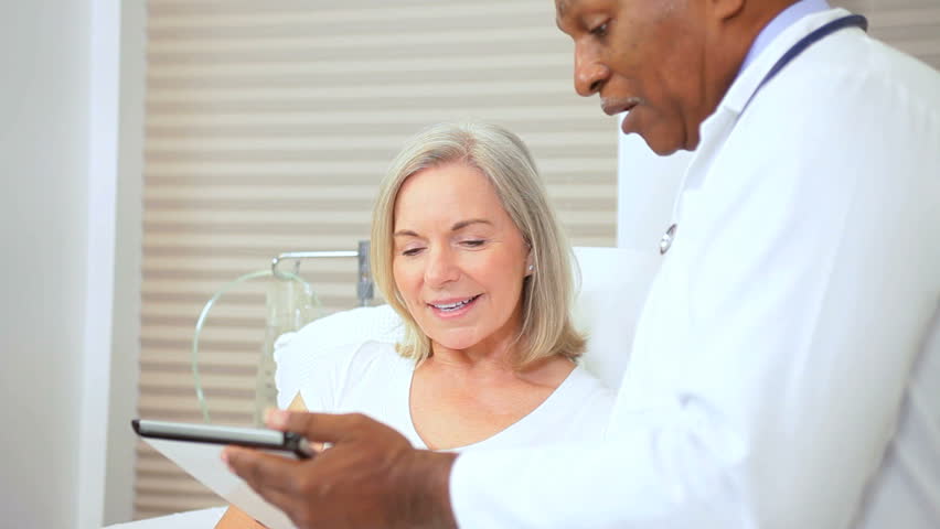 Ethnic medical consultant using wireless tablet inform senior female patient current treatment