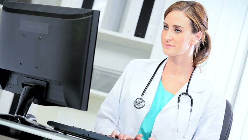 Female Caucasian hospital doctor using computer monitor to access data on clinical trials