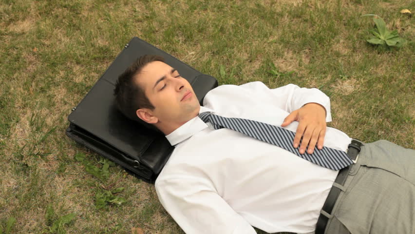 Close-up of a businessman sleeping on the lawn with briefcase as a pillow
