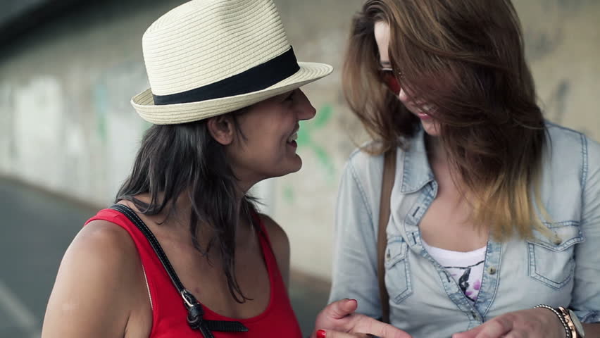 Female friends with smartphones standing in front of the wall, steadycam shot
