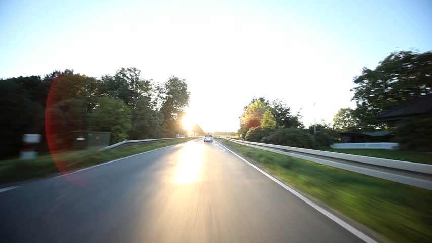 video footage of a on-board camera on a car driving on a country road in the sunset