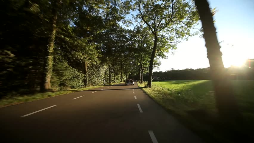 video footage of a on-board camera on a car driving on a country road in the sunset