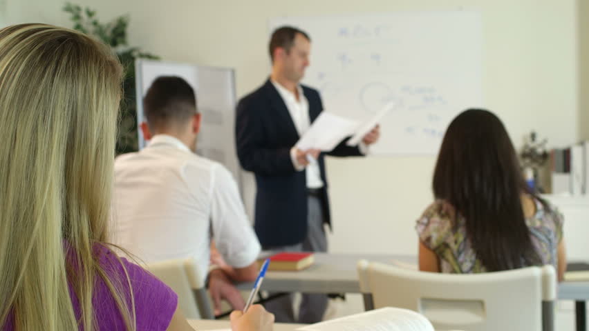 Instructor and other students turn their attention to a blond girl in the back of the room asking a question. rack focus shot.
