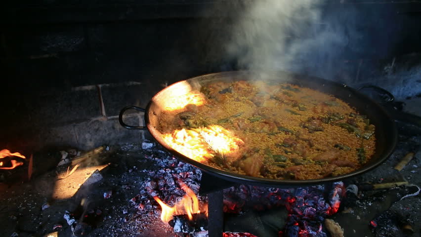 preparing large dish of paella with firewood