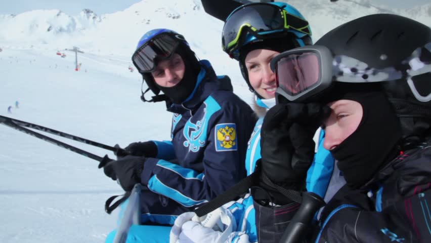 Three riders in helmets and goggles ride on cableway at mountains