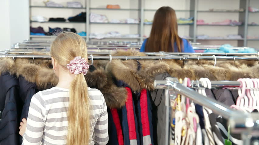 Mother and daughter shopping for girls clothes in a clothing store, child looking warmest jacket