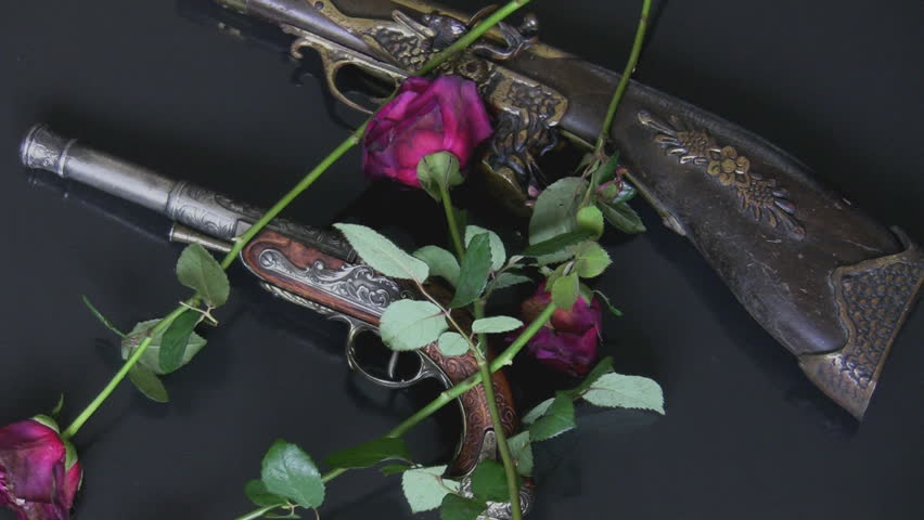 Withered red roses are falling on two old retro guns on a dark grey background