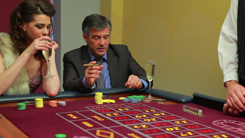 Woman drinking champagne and man smoking cigar placing bets on roulette table in the casino