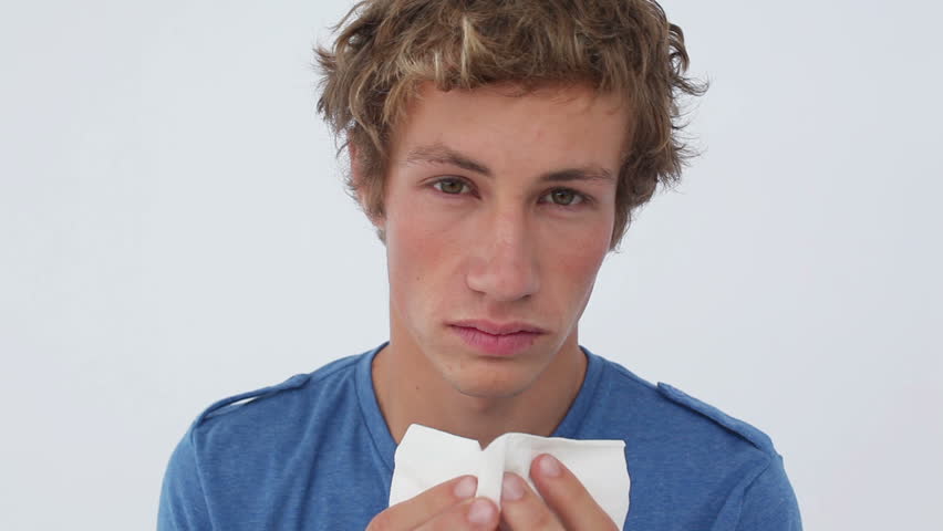 Sick man sneezing into a tissue against a white background
