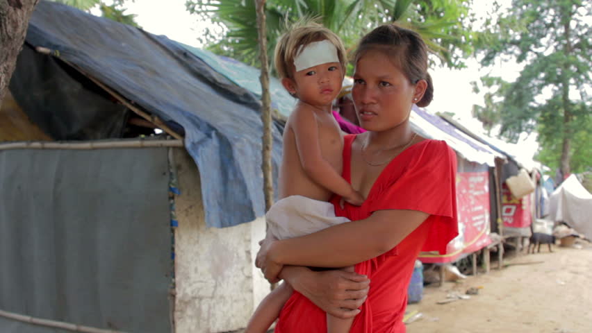 Mother holding baby in Cambodian shanty, shacks in background