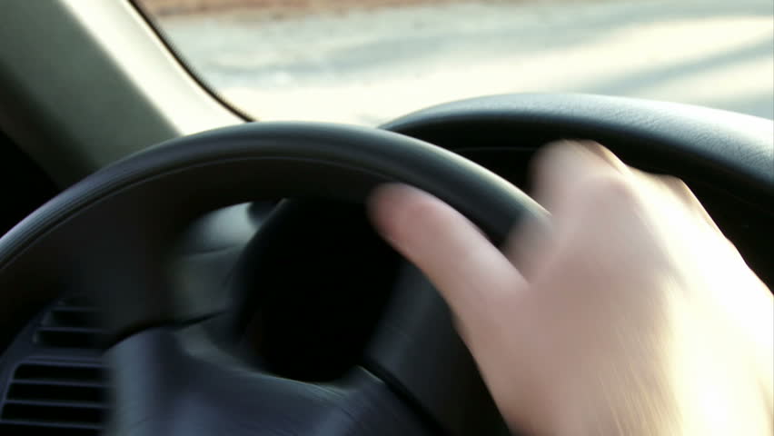Detail of hands turning steering wheel.