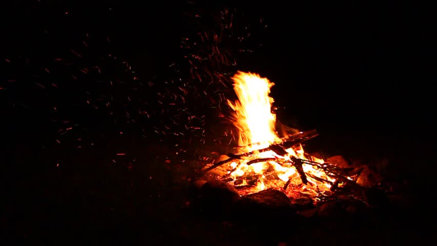 Flames of a cozy campfire flicker in a light breeze against a dark night