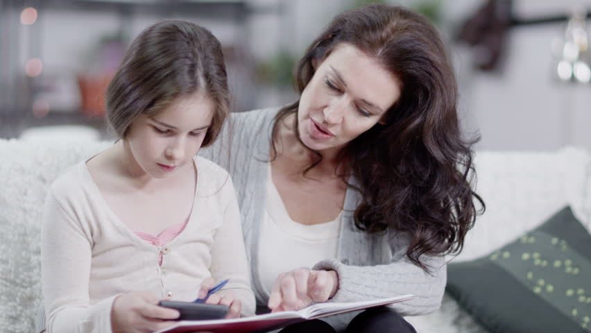 Caucasian mother with natural beauty helps her daughter to do her homework. In slow motion