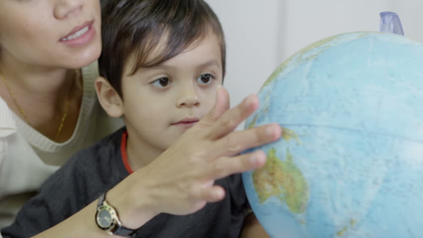 An attractive mother of Asian ethnicity uses a globe to show her young son the countries of the world. In slow motion.