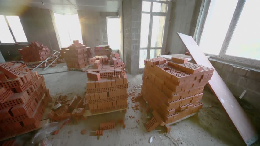 Stacks of red bricks inside unfinished room with sun light from windows, shown in motion