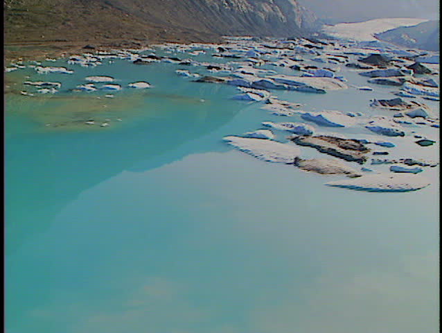 Low level fly over alpine lake filled with melting icebergs from mountain glacier