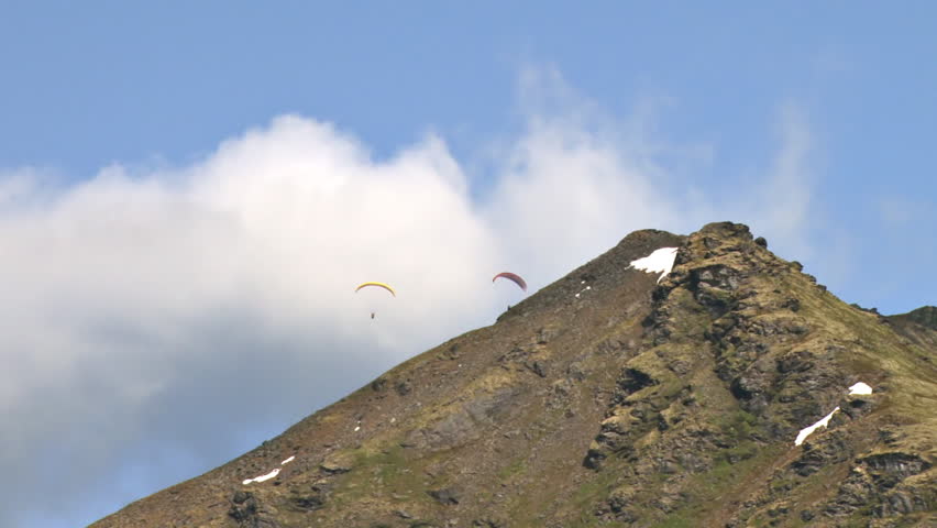 Paragliders soaring gracefully above the mountain ridges of Hathcer Pass in the Talkeetna Mountain Range in Alaska. Gentle tracking pan.