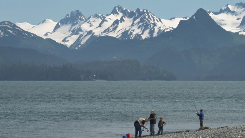 Kenai River, AK - CIRCA 2011: Fishermen onshore at Land's End fish, a boat passes by, and birds fly around in the air, all the while under the watchful gaze of the Kenai Mountains across the bay.