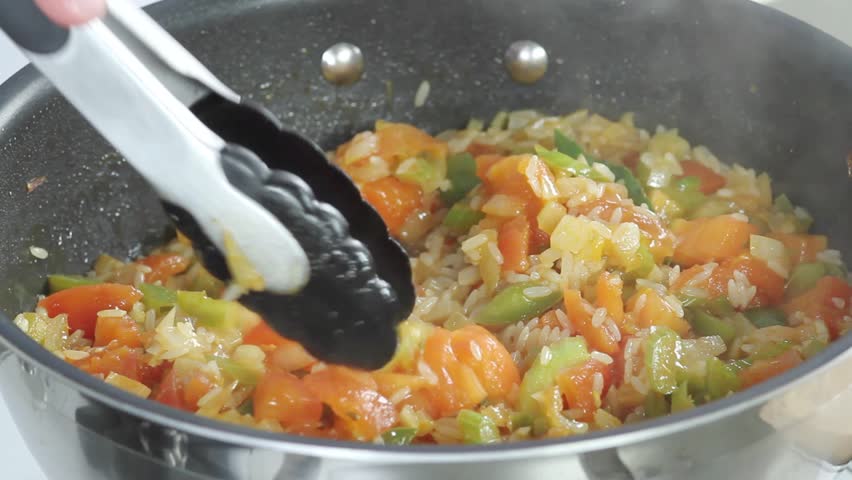 A simmering rice and vegetable stew being seasoned with salt and ground black pepper