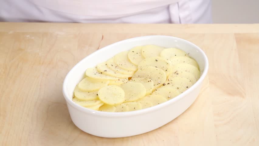 Cream being poured over potato slices in a baking dish
