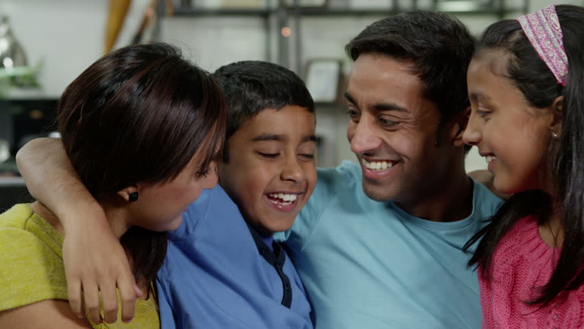 Happy family of 4 seated together at home. They are laughing and hugging.