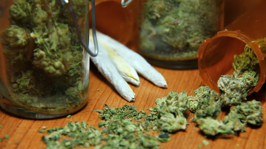 Cannabis and Smoke 3. Nuggets of marijuana, glass jars, prescription bottles and rolled joints on a table, puffs of smoke being blown.