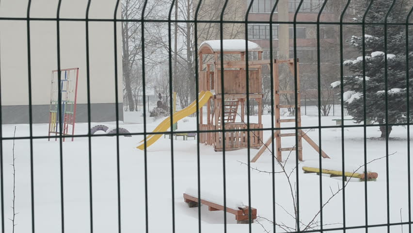 playground and other kindergarten toys in winter over fence. snowstorm blizzard snow fall.