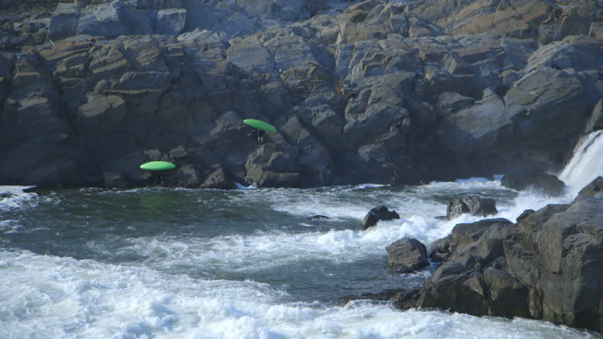 Finished with their run over the waterfall in the river two kayakers begin hauling their kayaks up the boulders that make up the riverbank.