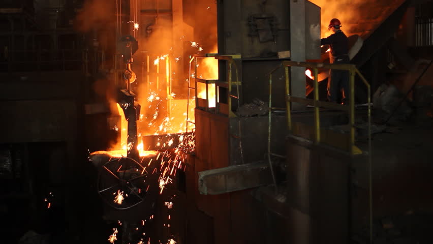 Hard work in the foundry, worker controlling iron smelting in furnaces, too hot and smoky working environment