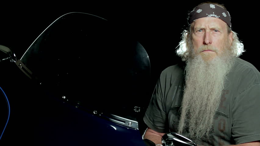 Mature Biker sitting on his motorcycle and looking mean and then smiling.