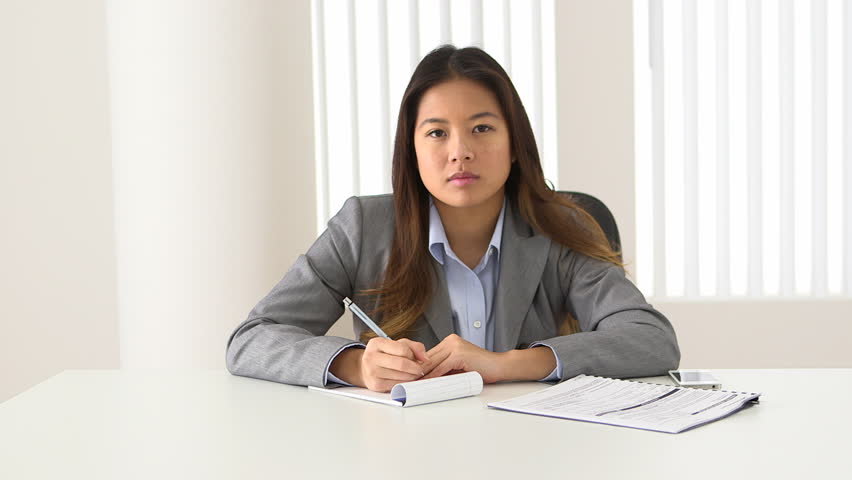 Asian businesswoman listening and taking notes during video conference