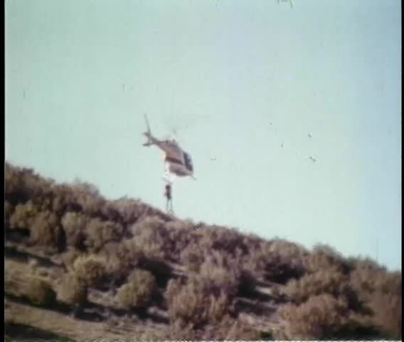 Stunt man hanging onto landing gear of helicopter in flight