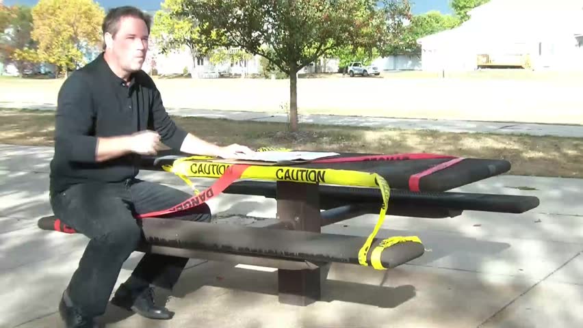 Single guy sits at outdoor table with yellow and red caution and danger tape surrounding, chewing pizza, and then opening box reading single, date me.