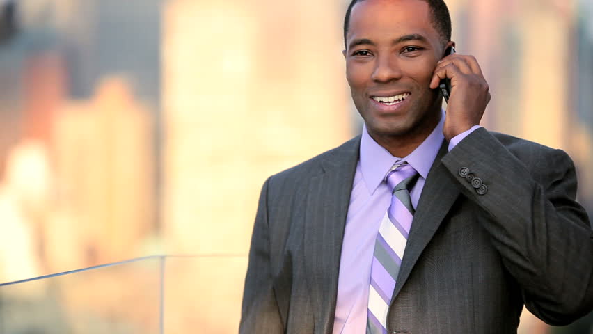 African American male business manager on a cell phone on rooftop overlooking NYC
