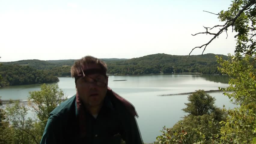 Lost business man in wilderness with beautiful lake view atop hill in background.