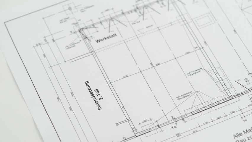 A hand is putting down two rolled blueprints and a regular compass