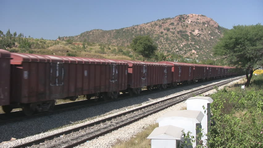 A Freight train is passing by a rural station in India.