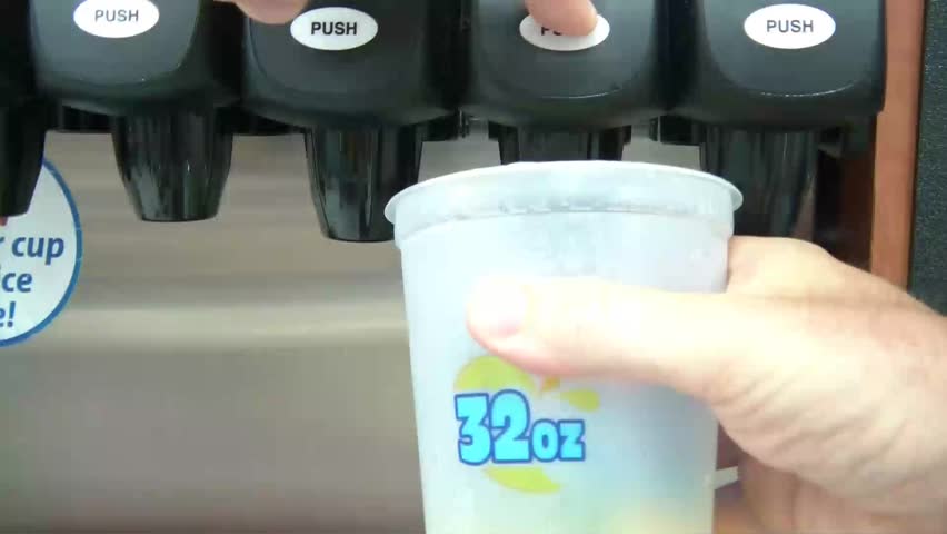 Hand fills up cup with soda at fountain machine by hitting plastic against lever.