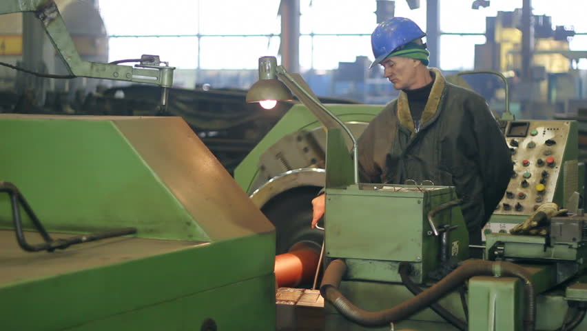 Worker on a machine, processing steel on a lathe in factory