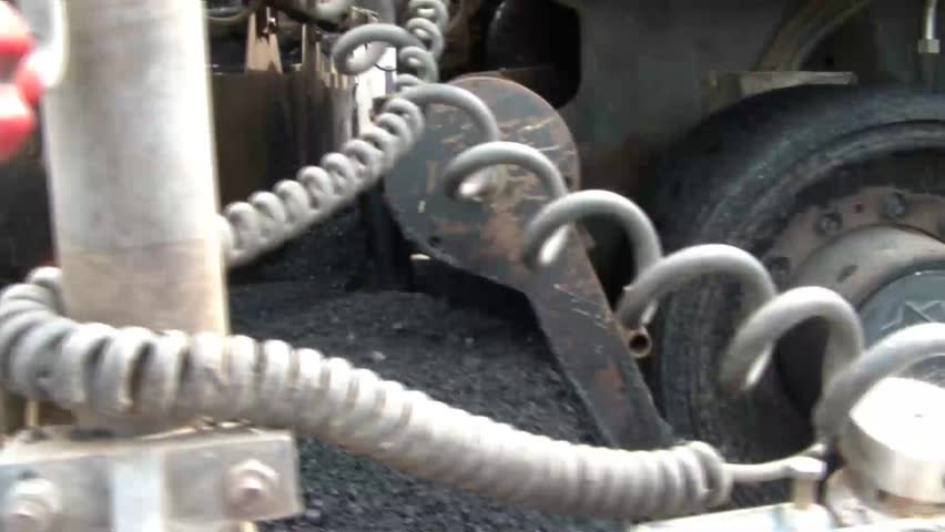 Clip of blacktop asphalt laying machine as it slowly goes by, the inner workings of tar being churned up, to the men who stand on back with smoke all day.